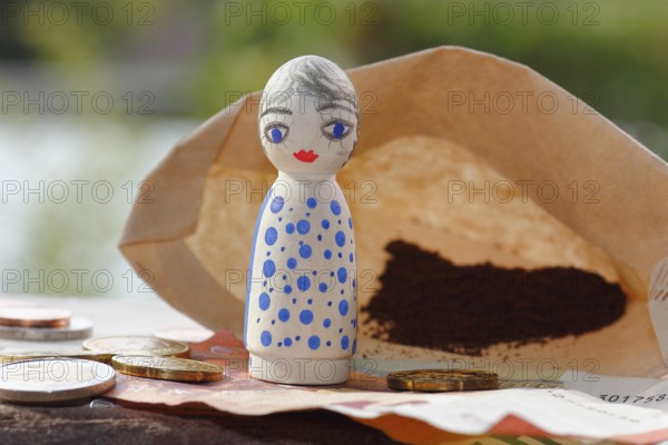 Pretty female wooden cone figure with coins and banknote in front of filter bag with coffee North Rhine-Westphalia, Germany