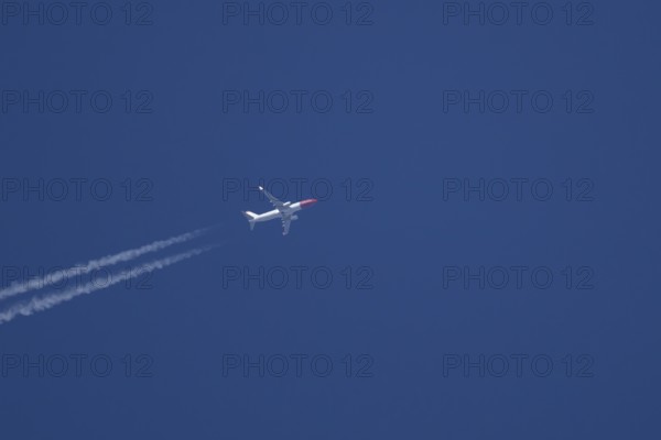 Boeing 737 jet passenger aircraft of Norweign Air with a vapour trial or contrail behind flying in a blue sky, England, United Kingdom