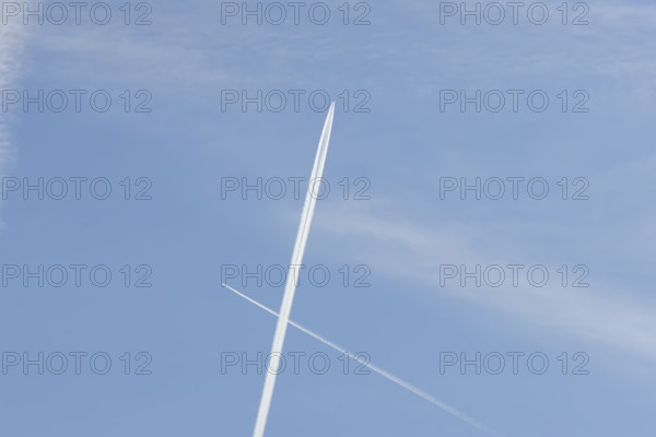 Two jet passenger aircraft with vapour trails or contrails flying in a blue sky crossing making a cross, England, United Kingdom