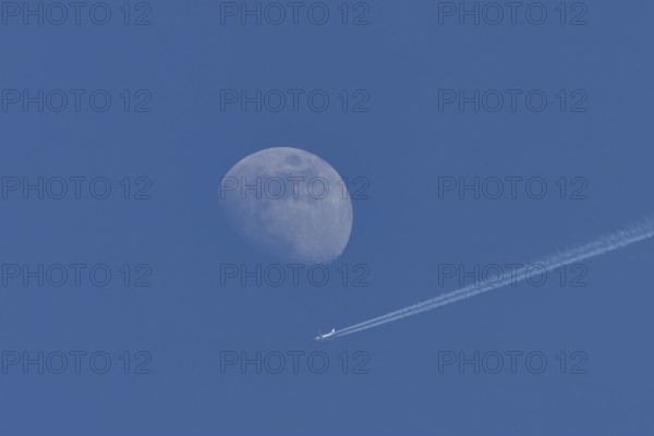 Boeing 737 jet passenger aircraft of Norweign Air with a vapour trial or contrail behind flying in a blue sky passing by the moon, England, United Kingdom