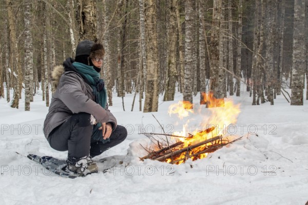 A woman warms herself by a campfire in winter, Gaspesie national park, Province of Quebec, Canada, north America