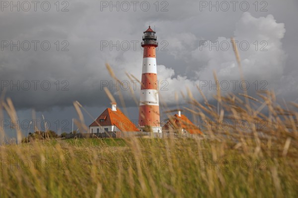Illuminated Westerheversand lighthouse on the North Sea under dark storm clouds