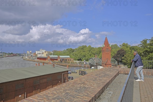 Tourist looking at the tower of the lift bridge and shed 8 at the Hansa harbour, Stadttrave, Marstallweg, Old Town, Lübeck, Schleswig-Holstein, Germany