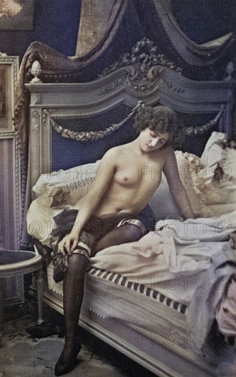 Female nude from around 1899, erotic postcard, Playgirl, A woman sits thoughtfully on a bed in a retro bedroom, coloured, reproduction from a photo around the turn of the century, Historical, digitally restored reproduction of an old original, exact date unknown