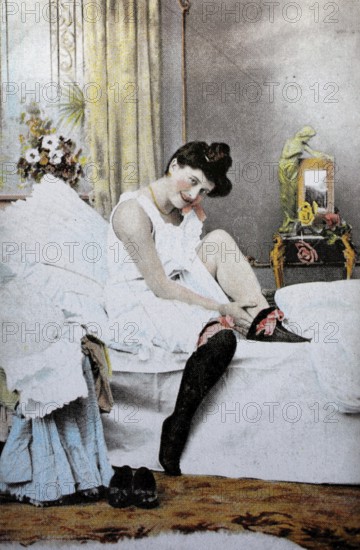 Female nude from around 1899, erotic postcard, playgirl, woman putting on stockings in the bedroom, emphasises relaxed and intimate domestic atmosphere, coloured, reproduction of a photo from around the turn of the century, historical, digitally restored reproduction of an old original, exact date unknown