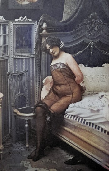 Female nude from around 1899, erotic postcard, Playgirl, A woman in a nude corset sits on a bed in a retro bedroom, coloured, reproduction from a photo around the turn of the century, Historical, digitally restored reproduction of an old original, exact date unknown