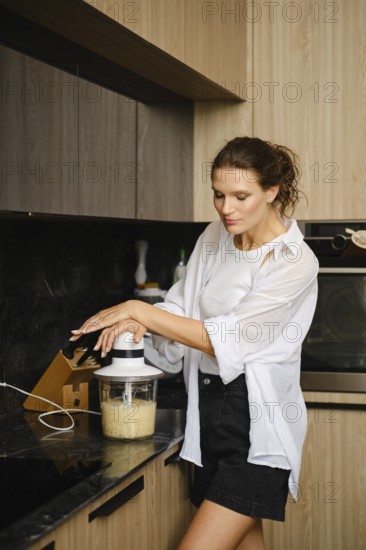 A woman skillfully blends banana and sea buckthorn fruits in a sleek kitchen. She carefully operates the blender, focusing on creating a healthy smoothie