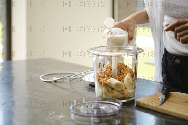 Ingredients are being added to a blender for smoothies. A person is pouring milk into the container filled with ripe bananas and sea buckthorn
