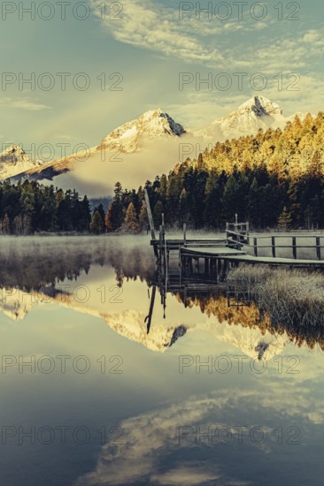 Lake Staz near Sankt Moritz in the Engadin in Switzerland. Morning atmosphere with fog in autumn. Water reflection and snow-covered mountains in the background