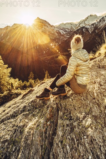 Woman sitting thoughtfully at a feslen at autumn atmosphere during sunset in the Swiss Alps in the Engadine. Photographed from the village of Maloja on the Maloja Pass