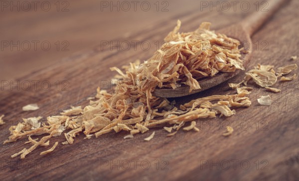 Smoked onion flakes, on a wooden spoon, wooden table, close-up