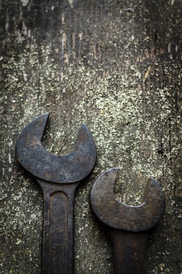 Two old, rusty wrenches rest side by side on a weathered wooden surface, highlighting their wear and the dedication to craftsmanship in a workshop setting