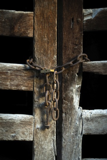 The wooden door, weathered and aged, is closed off with rusty chains, creating an intriguing contrast against the dark background, evoking a sense of mystery and history