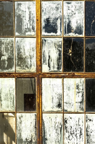 Cracked and peeling window panes reflect light and nearby objects, creating an atmosphere of nostalgia in an aged interior that tells a story of time and warmth