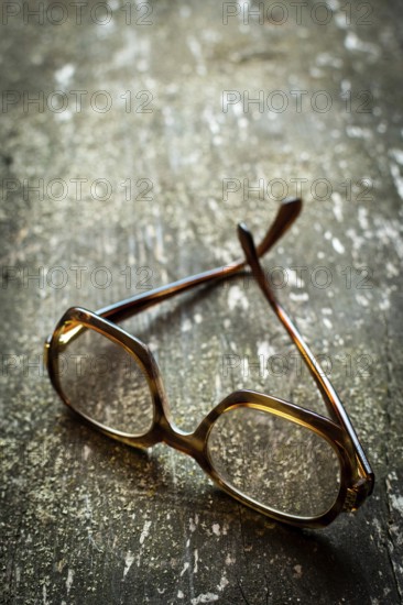 A pair of vintage glasses lies on a weathered wooden surface, enhanced by warm natural light reflecting off the delicate lenses, creating a serene atmosphere