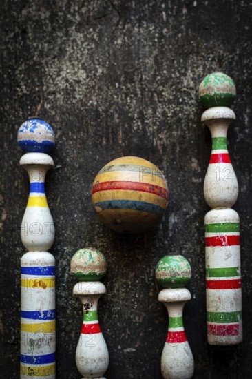 A classic bowling game set showcases worn wooden pins in vibrant colors and a striped ball, displayed on a rustic surface that enhances the nostalgic atmosphere for friendly competition