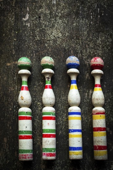Four vintage wooden bowling pins with vibrant colors sit in a row on a rustic wooden surface, showcasing their charming, worn look in a cozy indoor ambiance