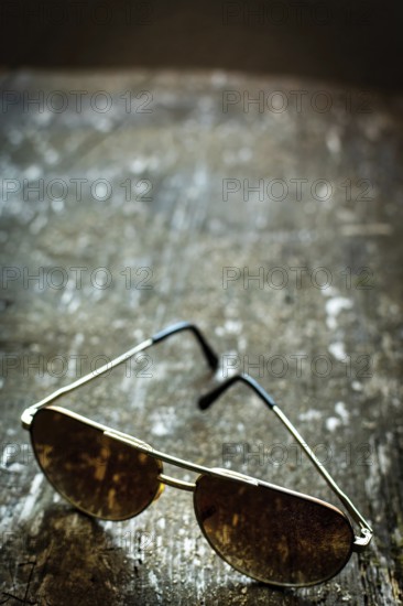 Sleek sunglasses rest on a weathered wooden surface, reflecting softly diffused light. The combination of the shades and rustic backdrop creates a timeless, stylish atmosphere