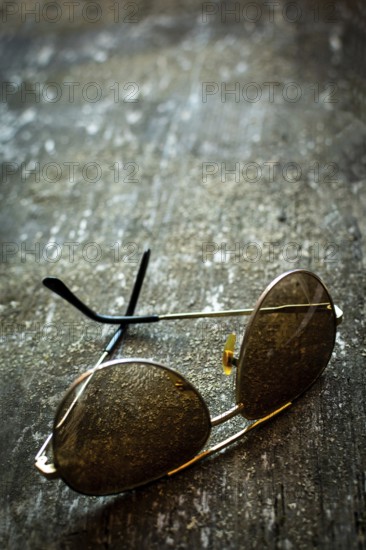 A pair of sunglasses lies on a rustic textured surface, capturing the essence of time. Warm light reflects off the lenses, enhancing the vintage atmosphere of the setting