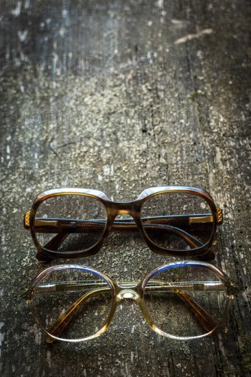 A collection of vintage eyeglasses rests on a rustic wooden surface, illuminated by warm lighting that highlights their unique designs and charm, evoking a sense of nostalgia