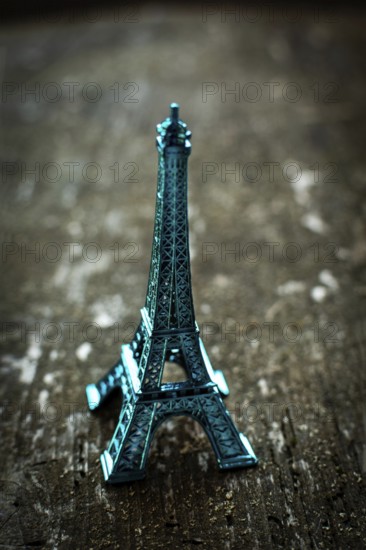 A striking teal miniature Eiffel Tower stands on a rustic wooden surface, bathed in soft lighting that enhances its unique vintage aesthetic, creating a charming ambiance
