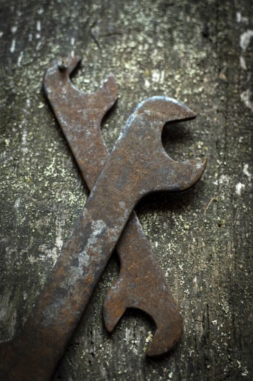 Two old wrenches rest crossed on a weathered wood surface, revealing their rust and signs of many years in mechanical work. The rustic backdrop emphasizes their vintage character