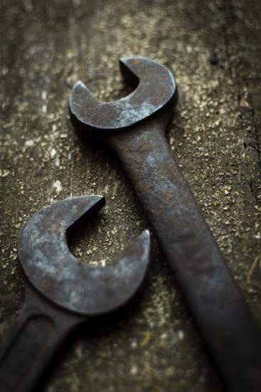 Two aged metal wrenches lie on a rugged wooden surface, illustrating their wear and the importance of tool upkeep in hands-on craftsmanship activities