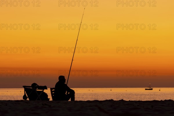 A man fishing just in front of sunrise on the Costa Rei, a coastline of the Italian island of Sardinia, in the Mediterranean Sea, Monte Nai, Costa Rei, Sardinia, Italy