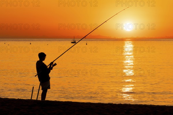 A boy fishing shortly after sunrise on the Costa Rei, a coastline of the Italian island of Sardinia, in the Mediterranean Sea, Monte Nai, Costa Rei, Sardinia, Italy
