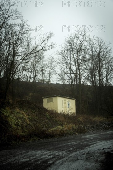 A small yellow building stands alone atop a dark hill, surrounded by bare trees. The atmosphere is moody and overcast, suggesting early evening or late afternoon. France