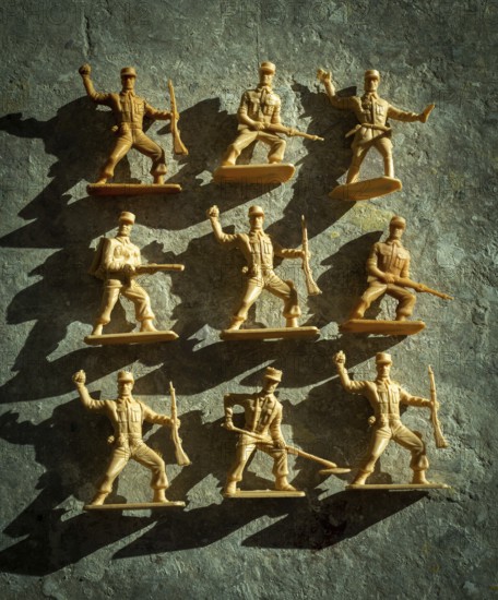 Plastic toy soldiers are displayed in different action poses on a textured surface, casting shadows that highlight their forms. Their playful arrangement evokes nostalgia and creativity