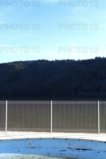 A swimming pool reflects the blue sky and surrounding mountains. A metal fence surrounds the space, accentuating the serene atmosphere during daylight
