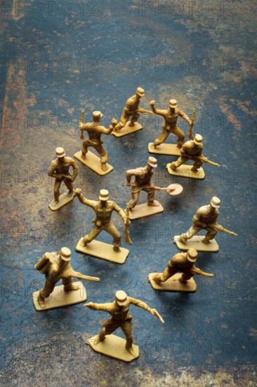 Small toy soldiers are positioned in a playful arrangement on a rough surface. Their poses suggest movement and action, inviting creative scenarios for playtime or collection
