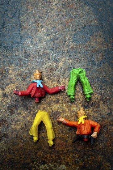 Four vibrant plastic figures with missing heads and different clothing pieces are creatively arranged on a rustic, textured surfaceFour vibrant plastic figures with missing heads and different clothing pieces are creatively arranged on a rustic, textured surface, highlighting their playful design