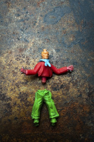 Brightly colored toy figure parts lie scattered on a rusted metal surface, showcasing a mix of red and green pieces, suggesting an ongoing toy repair or customization effort