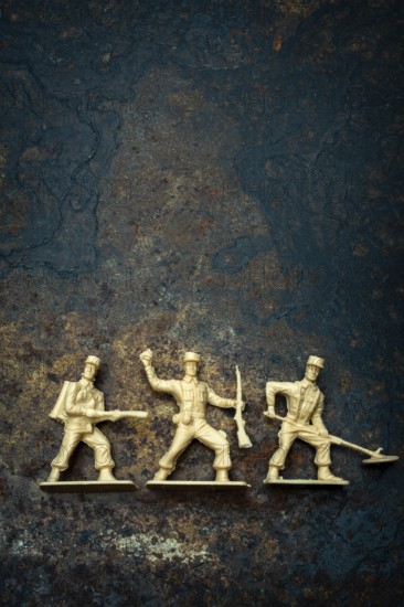 Three vintage toy soldiers in different poses rest on a rugged, textured surface. Their playful appearance evokes memories of childhood battles and imaginative war games
