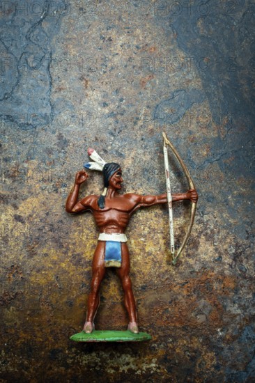 A bright plastic toy archer stands poised with his bow drawn back, showcasing the figure of an Indian Native American