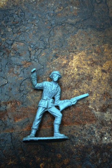 A vintage toy plastic soldier stands defiantly with a raised fist and a gun, symbolizing courage