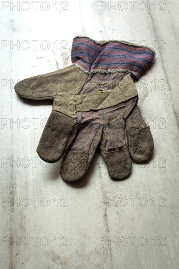 A leather glove, showing signs of age and wear, is placed flat on a textured wooden surface. The glove features a faded striped cuff, adding character to its rustic appearance