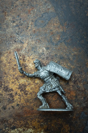 A roman soldier figure stands ready for combat, holding a sword in one hand and a shield in the other. The intricate design highlights historical