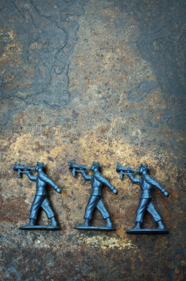Three small blue toy soldiers are positioned on a rough, textured surface, representing scenes from childhood games. Their sturdy posture and details trigger nostalgic memories of playtime adventures