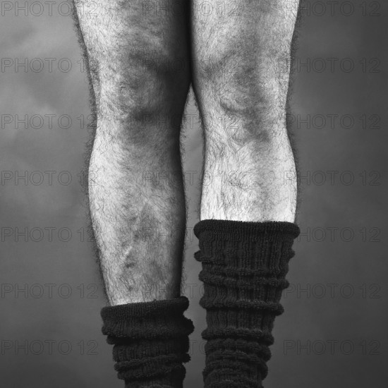 Close-up view of a pair of hairy male legs positioned together, wearing thick black mid-calf socks, suggesting a relaxed and casual indoor atmosphere during a laid-back moment