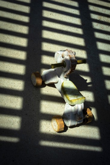 A vintage ride-on toy sits on a concrete surface, illuminated by sunlight streaming through a slatted structure, creating striking shadow patterns around it