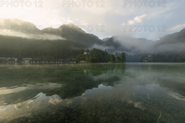 Mystical morning at Königssee in Schönau with boathouses and Christlieger. Sunrise and beautiful wafts of mist over the Königssee in the basin
