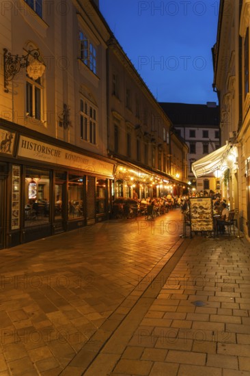 Cosy alley in the old town with illuminated cafés and historic pastry shop in Bratislava, Slovakia