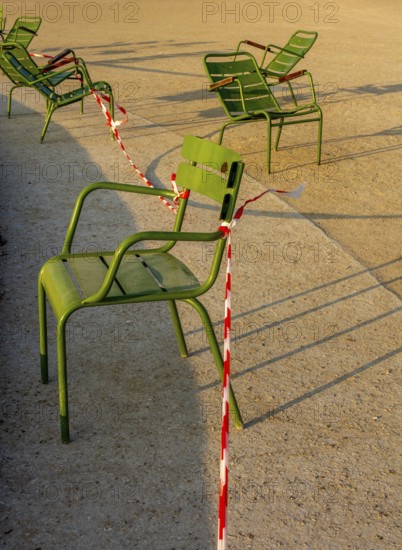 Several green chairs are placed next to each other in the sun at Tuileries Garden. Red and white caution tape surrounds one chair, indicating some areas may be restricted for visitors. Paris. France