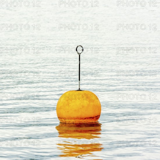 A bright orange buoy stands upright on the tranquil waters of Lake Geneva in Switzerland, surrounded by stunning natural scenery. Soft ripples reflect the buoy's color as it peacefully floats