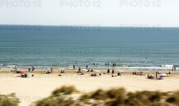 Sunbathers and swimmers relax on the sandy beach by the tranquil Mediterranean Sea. The atmosphere is lively with families enjoying their summer day in Herault, Occitanie, France