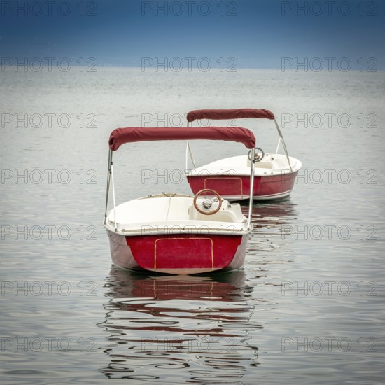 Several small red boats rest on the peaceful surface of Lake Geneva, reflecting the clear blue sky. The serene ambiance invites relaxation and enjoyment of nature in Switzerland