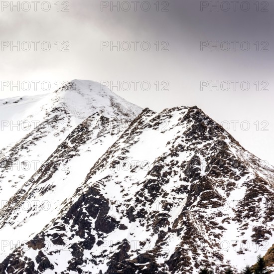 Snow-covered peaks of the Sancy massif rise dramatically against a moody sky in the Regional Natural Park of Auvergne Volcanoes during winter, showcasing the park's natural beauty. Puy de Dome. Auvergne Rhone Alpes. France